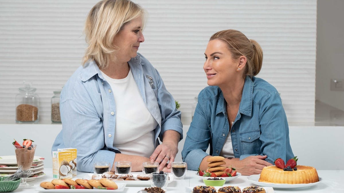 Two women sharing desserts and coffee at a table, smiling and enjoying each other's company.