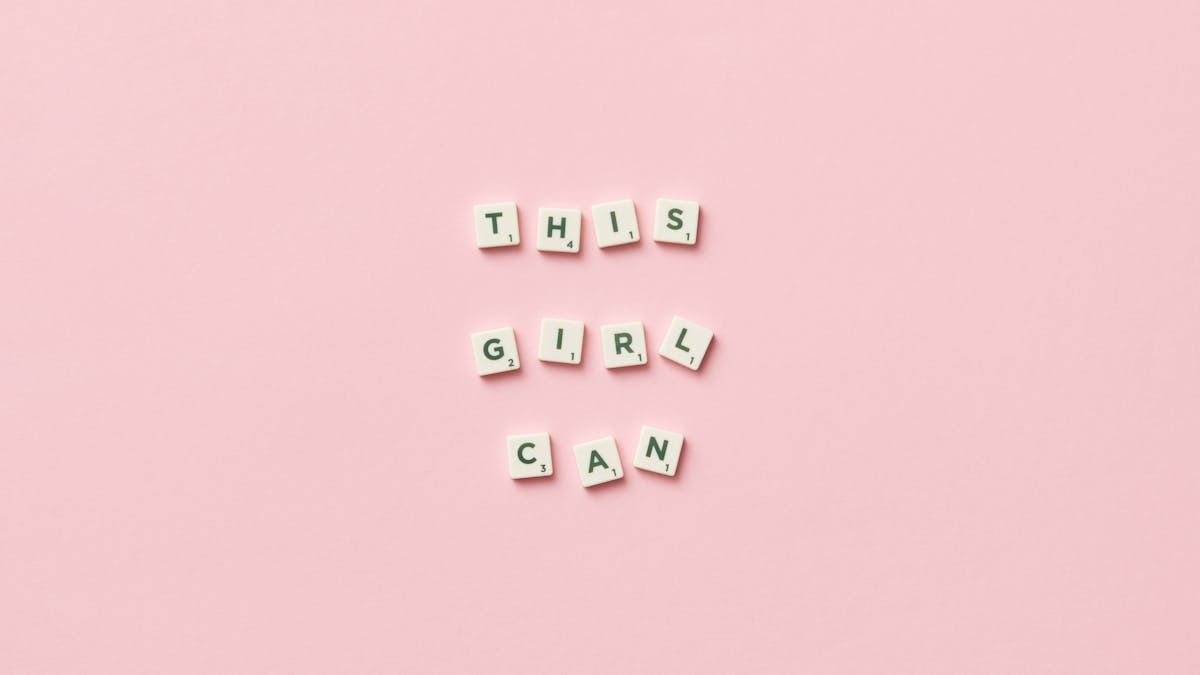 Scrabble tiles spelling 'This Girl Can' on a pink background.